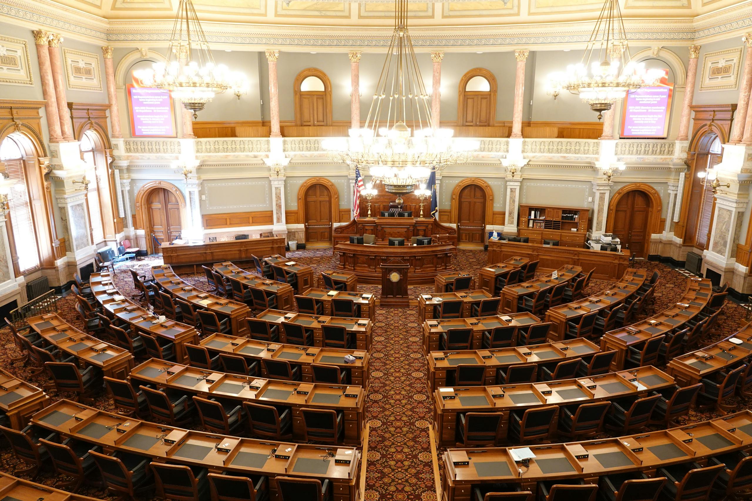 Wide view of an ornate legislative chamber with empty seats and chandeliers.